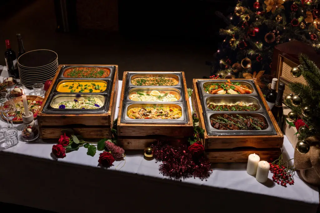 Warme gerechten van het kerstbuffet in warmhoudbakken naast de kerstboom